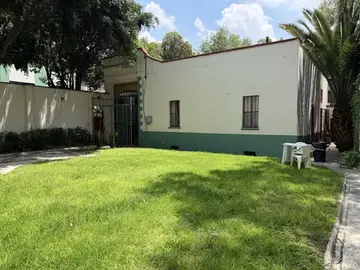 Jardín arbolado de Casa Popotla con césped y fachada blanca