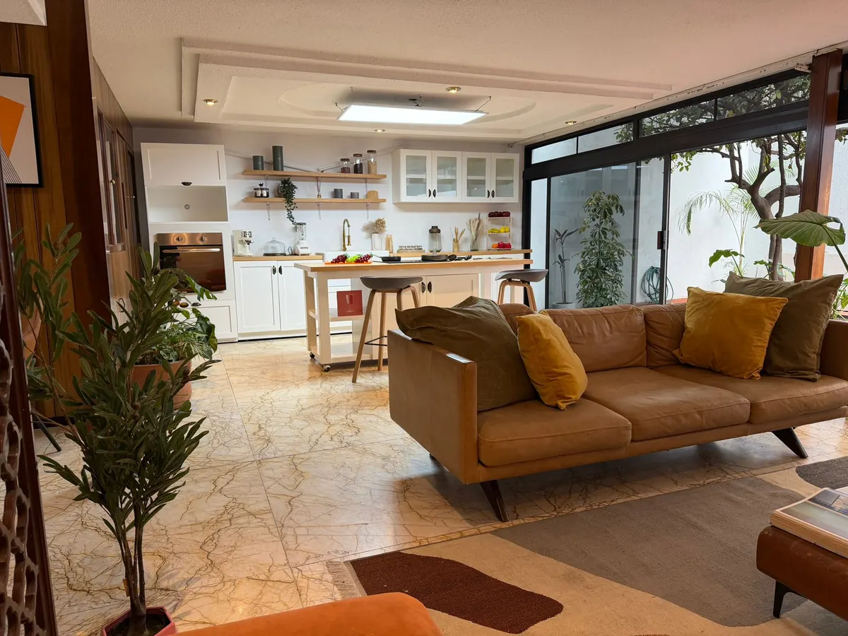 Sala de Casa Santa Mónica con sofá cálido, ventanales al patio y cocina al fondo